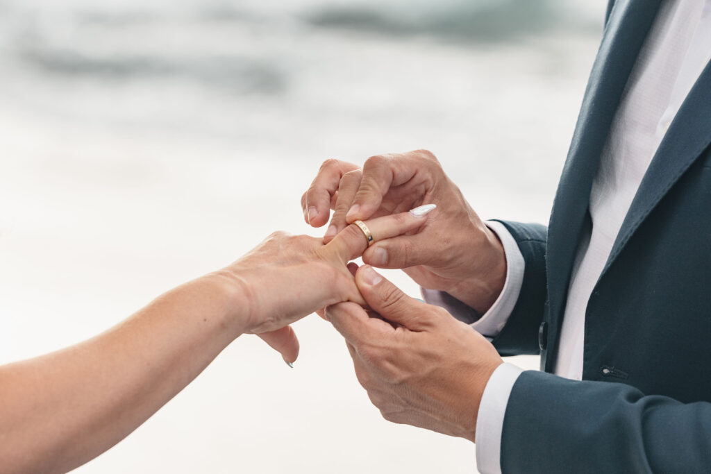 El símbolo del amor eterno: primer plano de dos manos durante la colocación de un anillo de oro en una ceremonia de boda al aire libre.