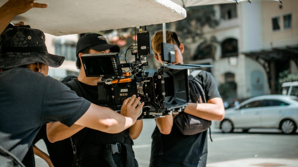 Equipo de filmación profesional trabajando al aire libre con una cámara RED montada en un rig estabilizador, ajustando el equipo y utilizando un reflector para controlar la luz. Este entorno es ideal para crear videos profesionales en Tenerife