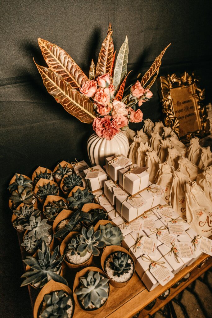 Detalles de boda originales: pequeños regalos y plantas suculentas en macetas, dispuestos sobre una mesa de madera rústica, junto con un arreglo floral y una tarjeta con la frase "Detalles para tus invitados"