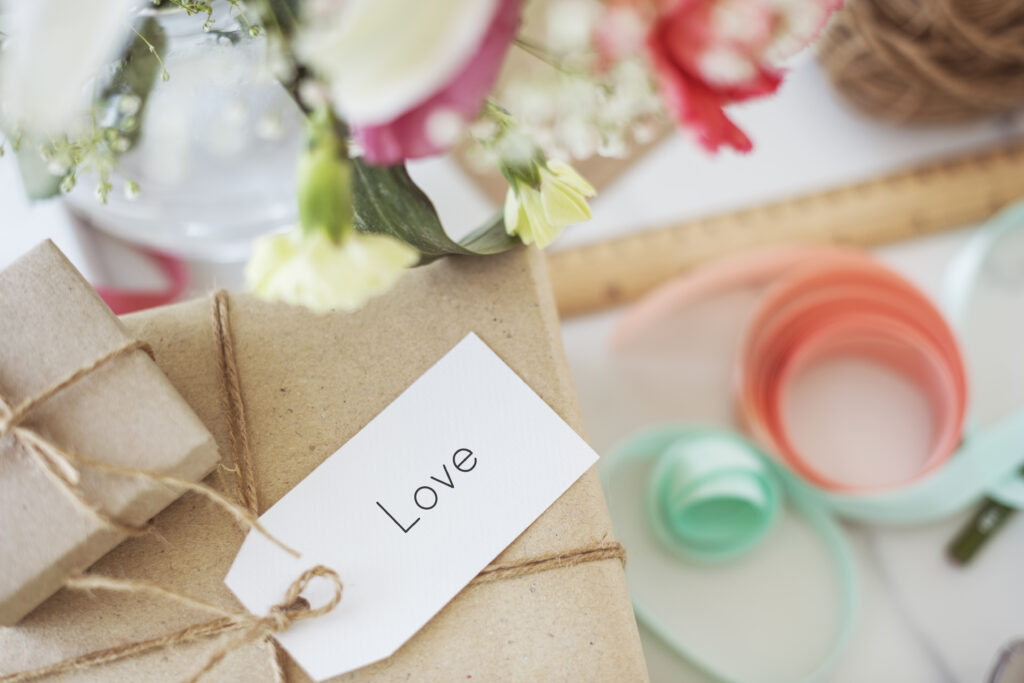 Detalle de boda original: un regalo envuelto con papel kraft y una etiqueta con la palabra "Love", sobre un fondo de elementos decorativos para boda.