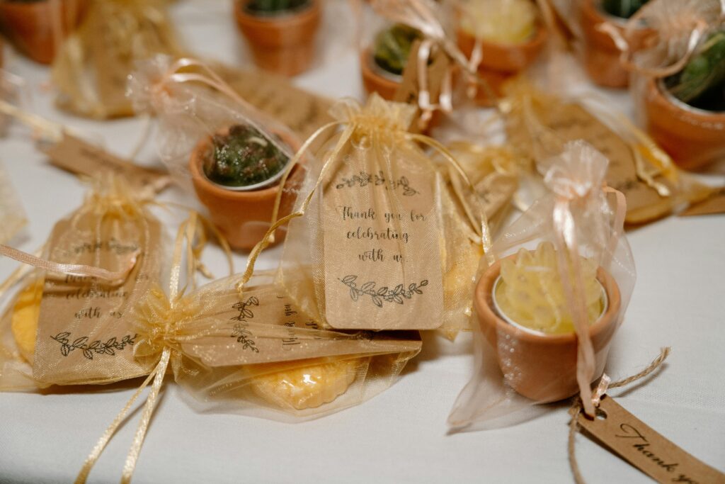 Regalos de boda únicos y personalizados: pequeños detalles envueltos en bolsas de organza con una etiqueta de agradecimiento "Thank you for celebrating with us", dispuestos sobre una mesa para los invitados.