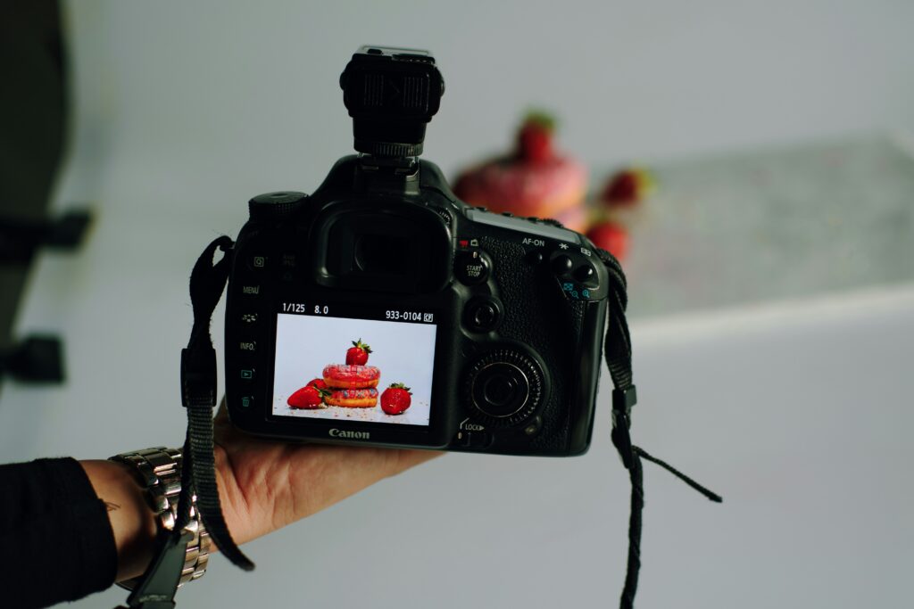 Fotografía de una mano sosteniendo una cámara réflex digital Canon con una pantalla que muestra una imagen de comida, un equipo esencial para la fotografía profesional de alimentos.