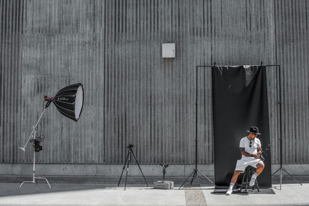 Configuración de fotografía profesional al aire libre con una persona sentada frente a un fondo negro, rodeada de equipo de iluminación y fotográfico.