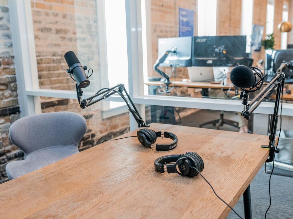 Estudio de podcast en Tenerife con dos micrófonos en brazos articulados, auriculares sobre una mesa de madera y ordenadores al fondo.